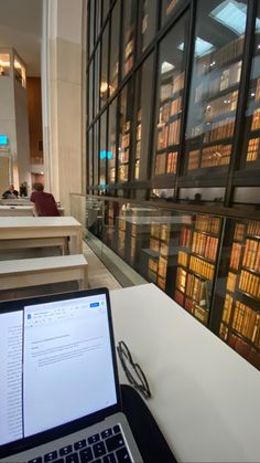 an open laptop computer sitting on top of a white table next to a library filled with books