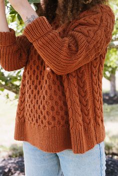 a woman in an orange sweater is taking a picture with her cell phone while standing under a tree