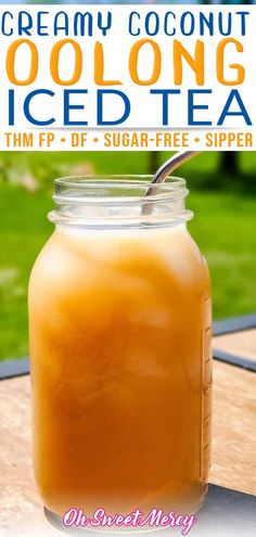 a mason jar filled with iced tea sitting on top of a wooden table next to a green field