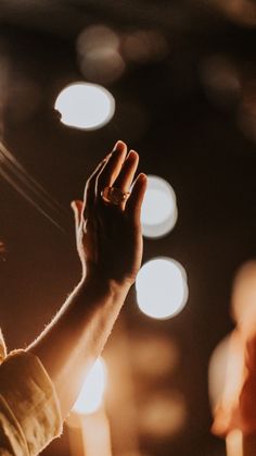 a person holding their hand up in the air with lights around them behind them and onlookers