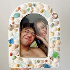 a man and woman are smiling in a frame made out of seashells