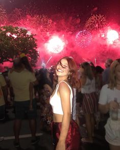 a woman standing in front of a crowd at night with fireworks on the sky behind her