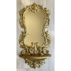 an ornate gold mirror on a shelf against a white tile wall with wood flooring