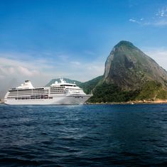 a large cruise ship in the ocean near a small island with a mountain in the background