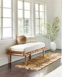 a white couch sitting on top of a wooden floor next to two windows and a rug