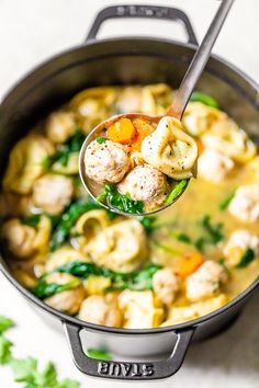 a ladle full of soup with meatballs and spinach