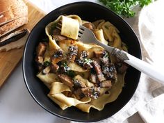 a bowl filled with pasta and meat on top of a wooden cutting board next to bread