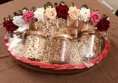 an arrangement of nuts and flowers in glass jars on a red tray with string wrapped around it