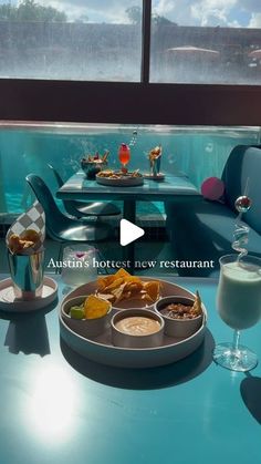 a table with food and drinks on it in front of a window that looks out onto the water