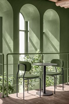 two chairs sitting at a table in an empty room with green walls and arched windows