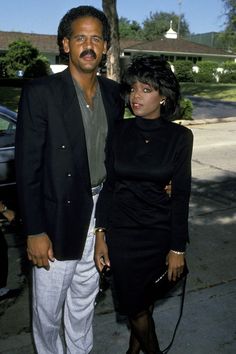 a man and woman standing next to each other on the sidewalk in front of a house