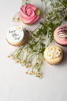 three decorated cupcakes sitting on top of a table next to flowers and greenery