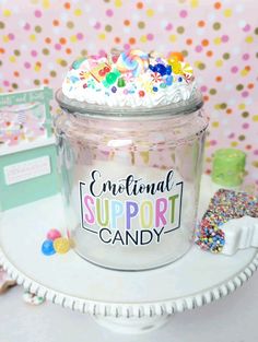 a glass jar filled with white frosting and sprinkles on top of a table