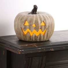 a carved pumpkin sitting on top of a wooden table next to a black dresser and white wall