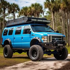 a blue truck parked on top of a dirt road next to palm tree covered forest