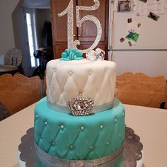 a three tiered cake with blue and white frosting on the top, sitting on a table in front of a refrigerator