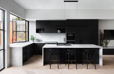 a modern kitchen with black cabinets and white counter tops is featured in this image, along with bar stools that match the hardwood flooring