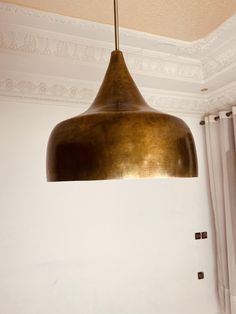 a large brass light hanging from the ceiling in a room with white walls and curtains