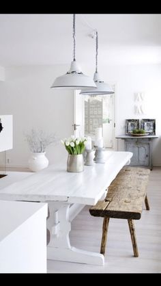 a white table and bench in a room with wood flooring, two lights hanging from the ceiling