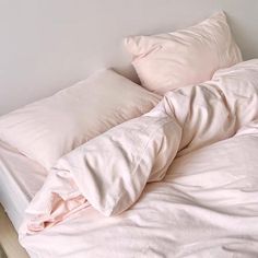 an unmade bed with pink sheets and pillows