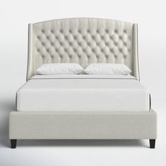 an upholstered bed with white sheets and pillows