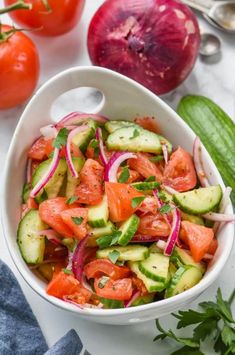 a white bowl filled with cucumber, tomatoes and onions next to other vegetables