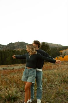 a man and woman are standing in the grass with their arms around each other as they look into the distance