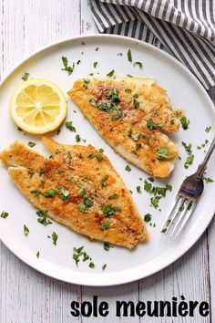 two fish fillets on a white plate with lemon wedges and parsley garnish