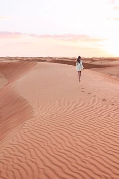 a woman walking in the desert at sunset