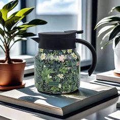 a glass tea pot sitting on top of a table next to a book and plant