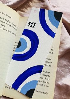 an open book laying on top of a bed next to a pink sheet with blue swirls