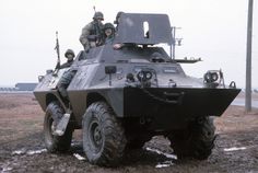 two soldiers are sitting on top of an armored vehicle in the mud while another soldier stands behind them