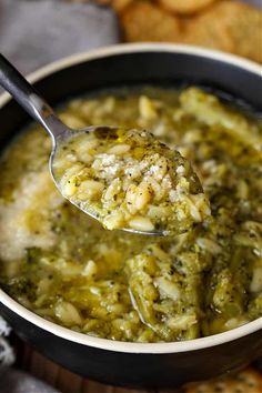 a spoon full of broccoli and cheese soup with crackers in the background