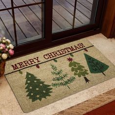 a merry christmas door mat with trees on it next to a potted plant and window