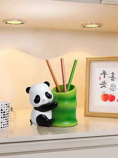 a panda bear figurine sitting next to a green cup with bamboo sticks in it