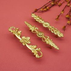 three pieces of gold colored metal on a pink surface