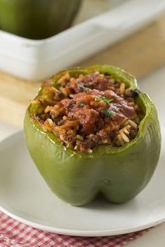 a green pepper stuffed with meat on a white plate next to an apple and a serving dish