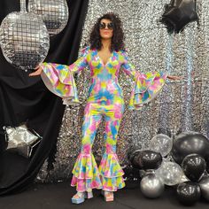 a woman standing in front of balloons and disco balls wearing a colorful outfit with bell sleeves