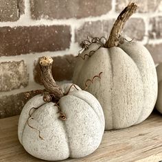 two white pumpkins sitting on top of a wooden shelf next to a brick wall