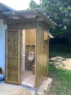 a wooden outhouse with a urinal in the door and a tiled floor next to it