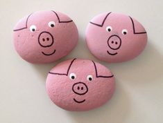 three pink rocks with faces painted on them sitting next to each other in the shape of pigs