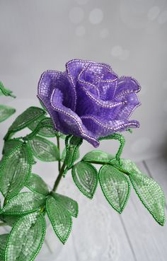 a purple rose with green leaves on a white table