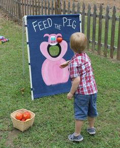 a young boy standing in front of a feed the pig sign with apples on it