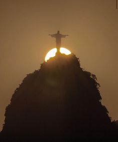 the sun is setting behind a statue on top of a hill in rio cristo