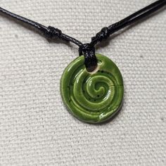 a green pendant with a spiral design on it's black leather cord is hanging from a white fabric