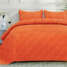 an orange bedspread and pillows in a white room with plants on the side