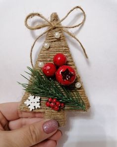 a hand holding a small christmas tree ornament with berries and pine cones on it