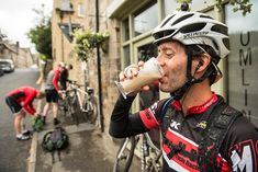 a man drinking from a bottle while riding his bike down the street with other bicyclists in the background