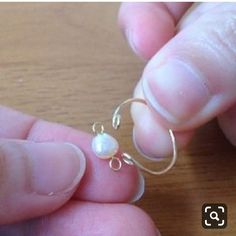 a person is holding a tiny white pearl in their left hand while wearing a silver earring