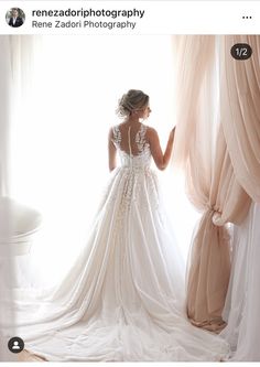 a woman standing in front of a window wearing a wedding dress and looking out the window